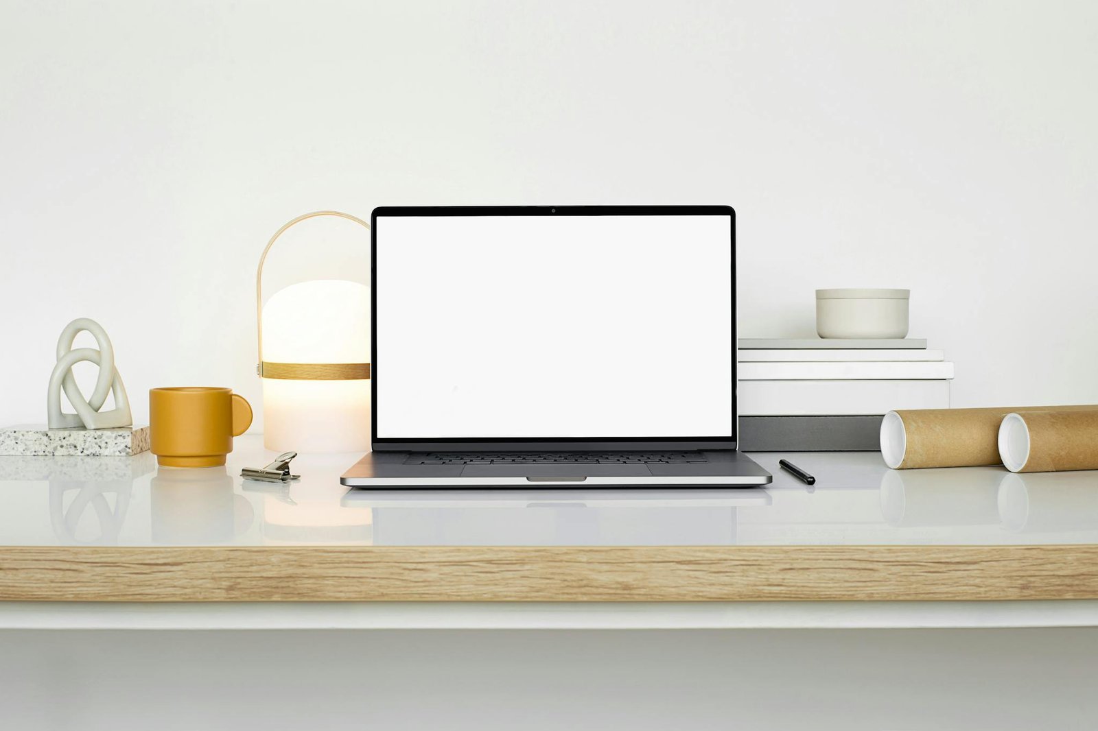 Sleek workspace setup featuring a laptop, mug, and decor on a white desk.
